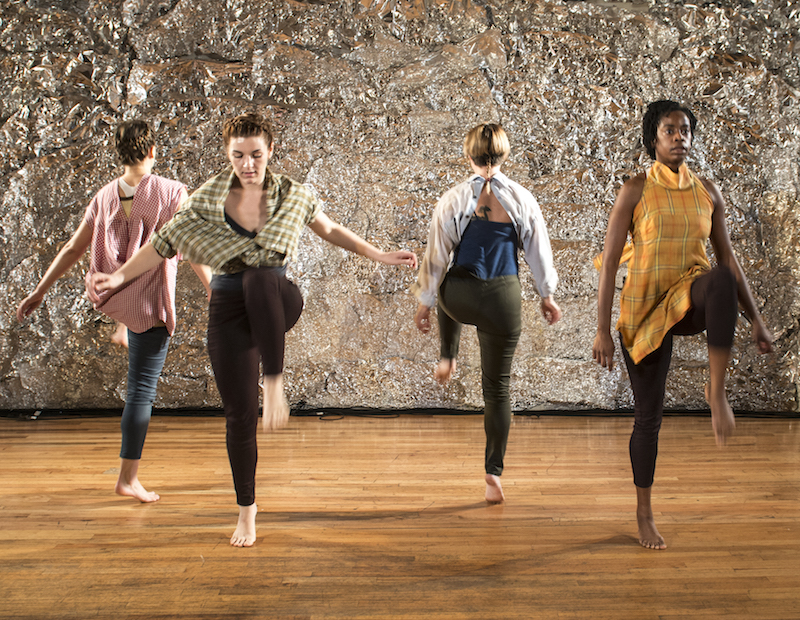 A quart of four dancers with their legs in the air at 90 degree angles. They look like they're hovering over the side of a building